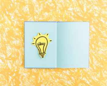 Idea Light Bulb On Blue Page Notebook Over The Yellow Textured Background