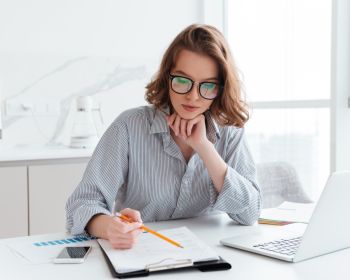 Young Concentrated Businesswoman In Glasses And Striped Shirt Working With Papers At Home