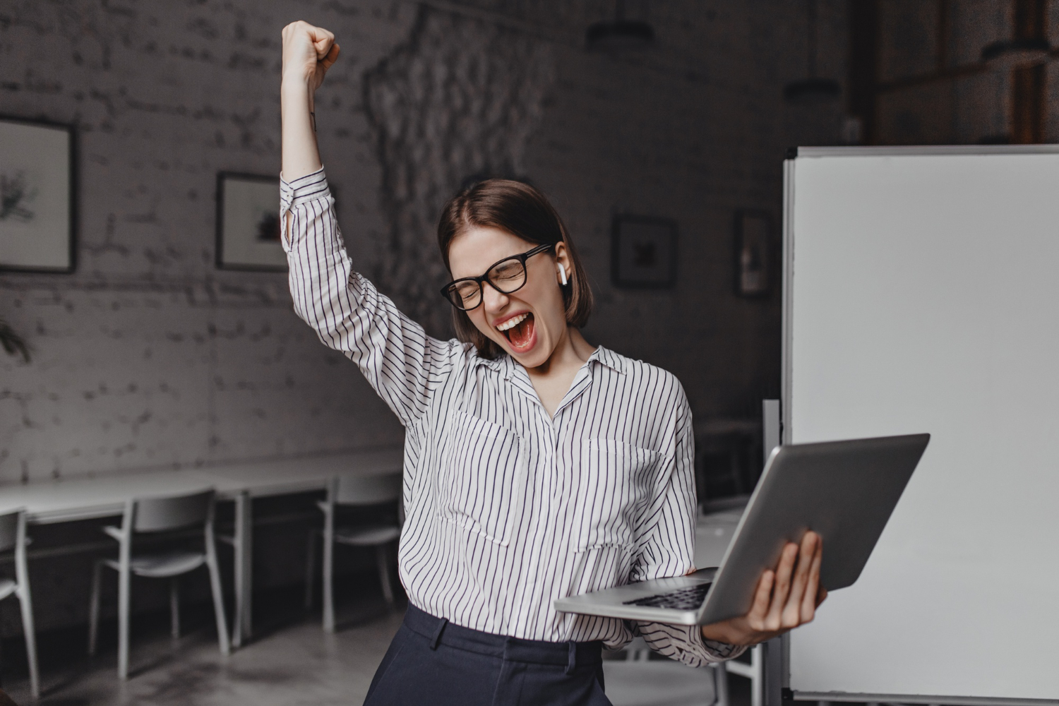 Business Woman With Laptop In Hand Is Happy With Success Portrait Of Woman In Glasses And Striped Blouse Enthusiastically Screaming And Making Winning Gesture